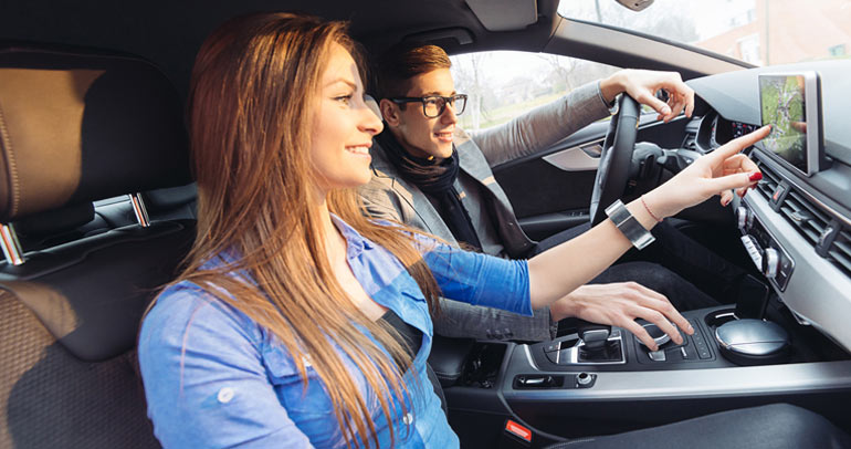 An image of a man and woman interacting with the screen in their electric vehicle (EV) while on a road trip