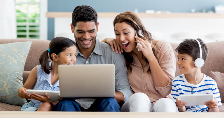A family, sitting on the couch using their technology devices for entertainment and communication