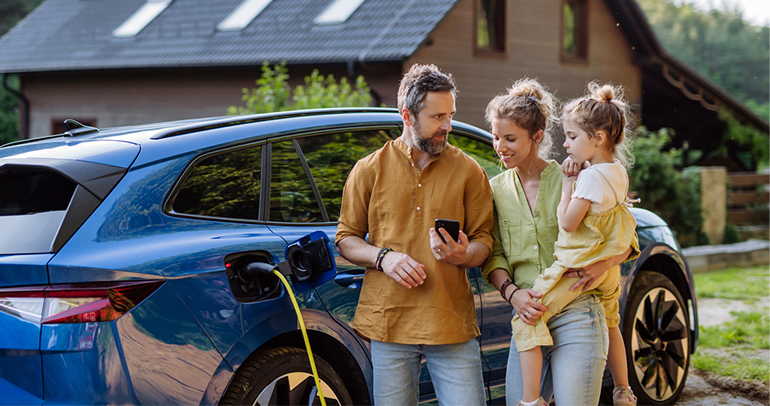 An image of a father, mother and child charging a BEV at home while checking out something on their smart phone.