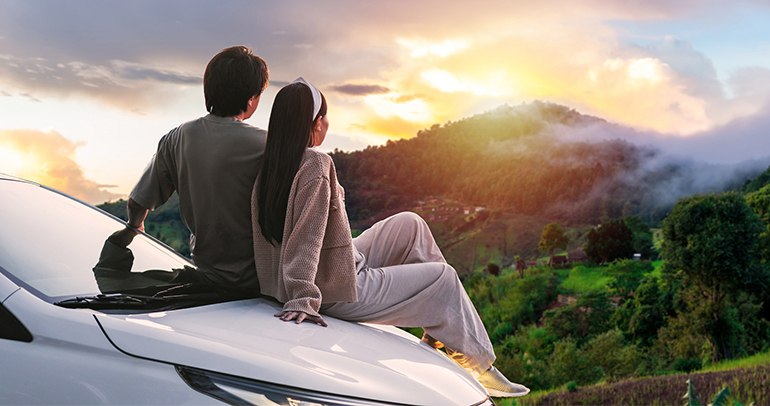 A young Southeast Asian couple looking at a sunset over a mountain in Thailand