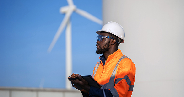 A utility worker is using a tablet for the utility's wind turbine sustainable energy project